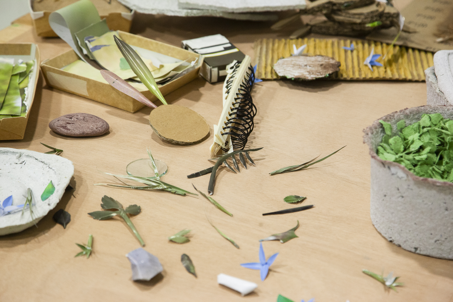 Photographie en gros plan de petits éléments posés sur une planche comme des morceaux de papiers découpés, des contenants en carton et en papier mâché.