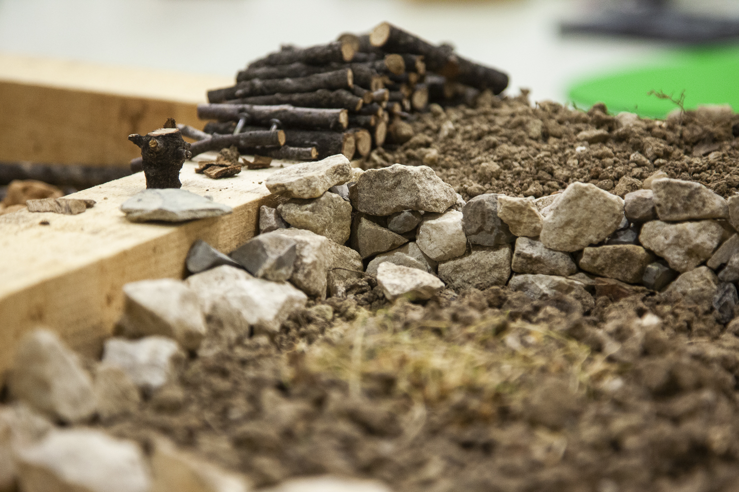 Photographie en gros plan d'une construction miniature (tas de bois et mur en pierre sèche).